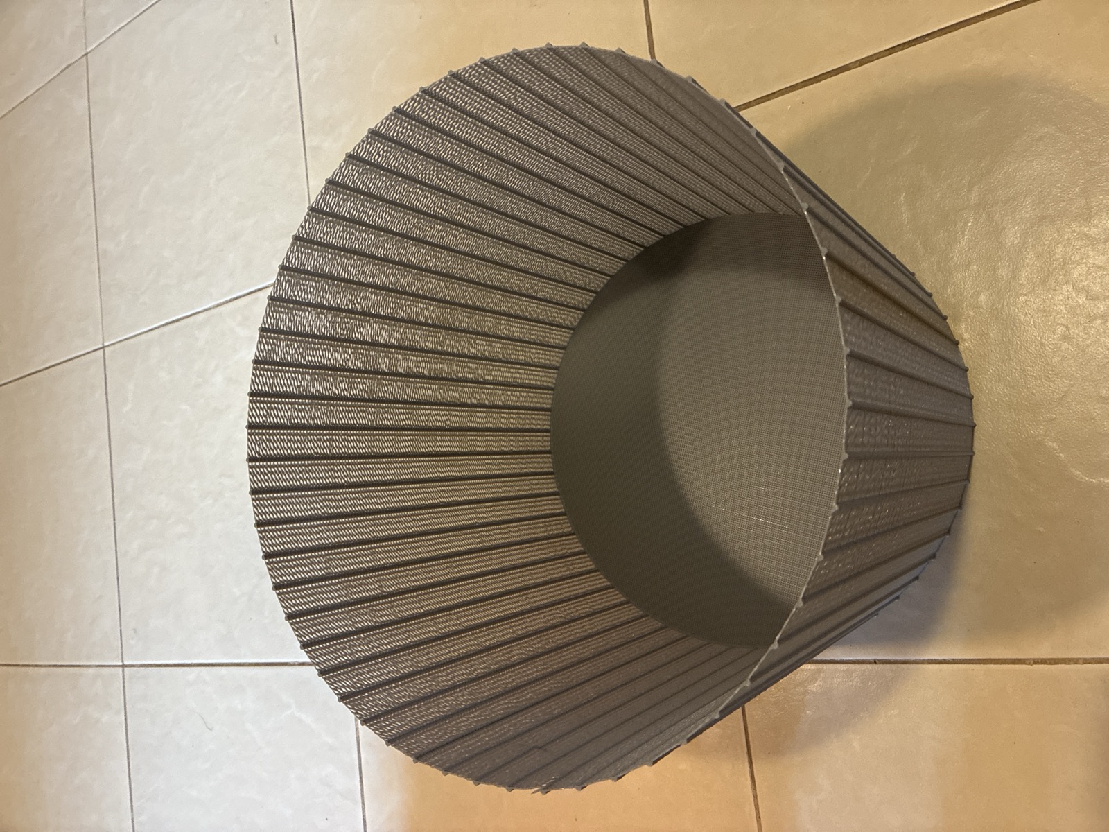 The finished 320 mm bucket seen from above, standing on a tiled floor: a complete fluted drum with a fine mesh floor visible inside