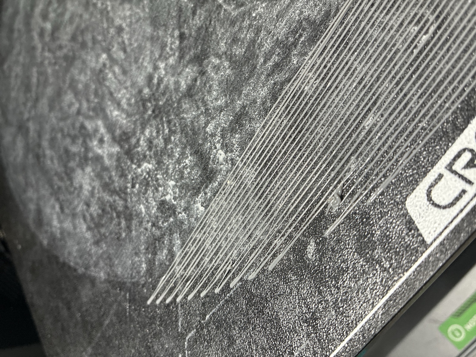 A failed base first layer: parallel extruded strands sitting loose on the dark build plate, several ends separated and lifting instead of welded into a sheet