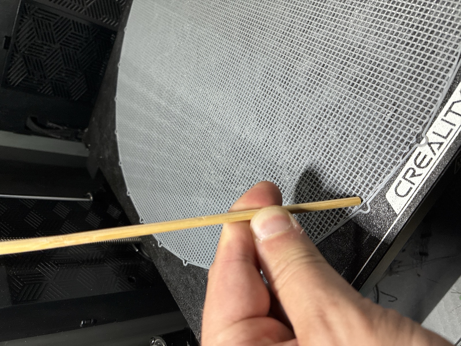 The printed floor disc as a fine cross-latch grid on the build plate, with a bamboo skewer held across it for scale