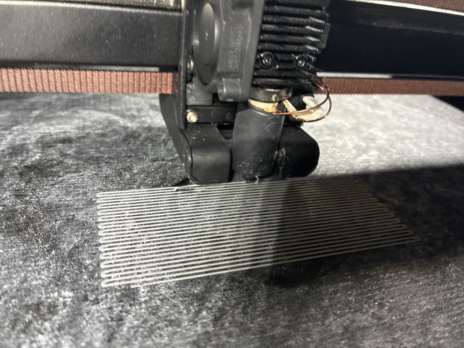 The printhead mid-print above a raster of first-layer lines, with a clump of stray filament clinging to the nozzle assembly
