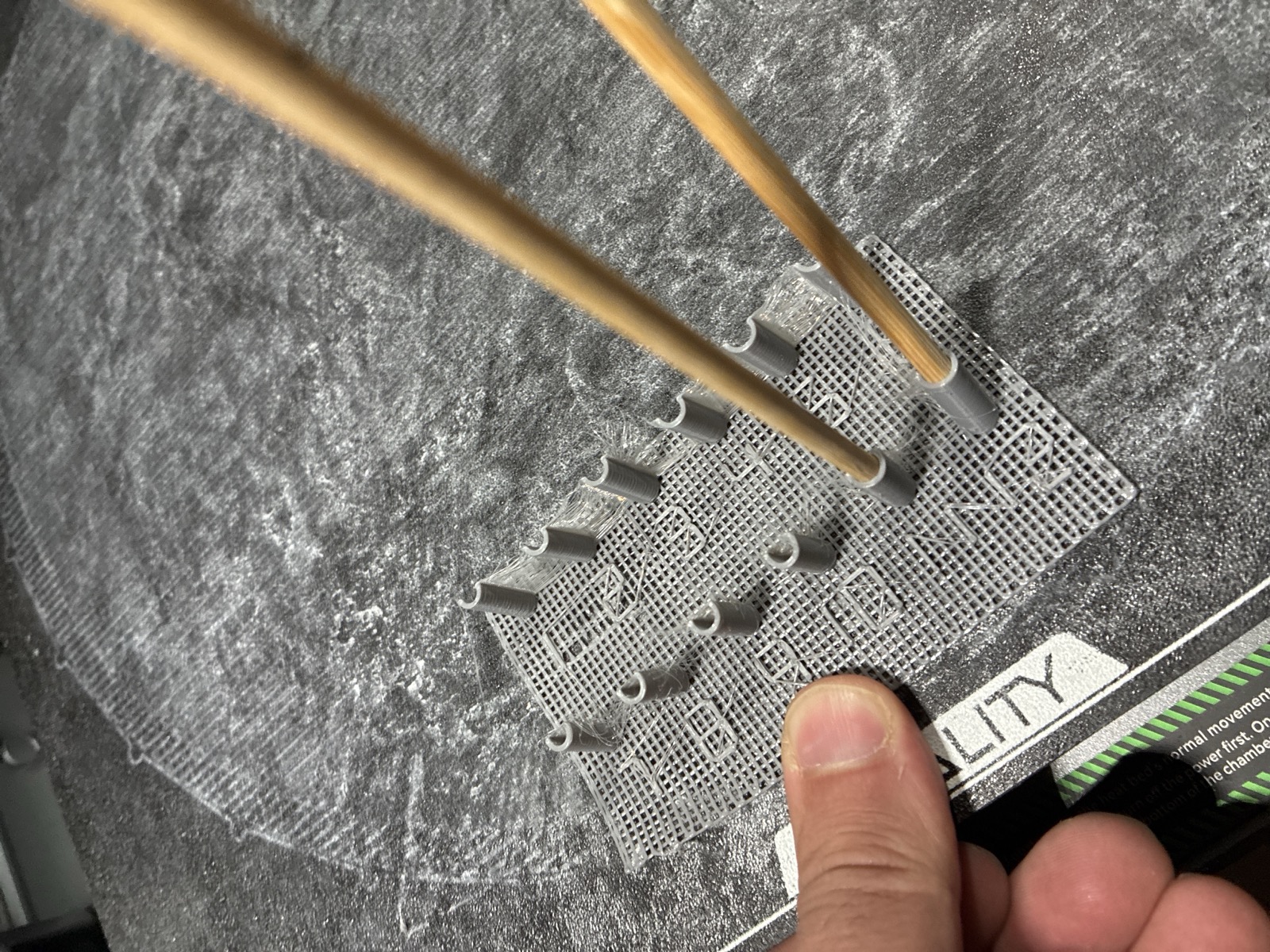 The printed bore gauge on the build plate: a mesh base carrying a row of C-channel posts at stepped bores, with two real bamboo skewers pushed into the cells that fit